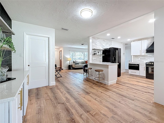 kitchen with a kitchen bar, black appliances, light wood-style flooring, tasteful backsplash, and wall chimney range hood