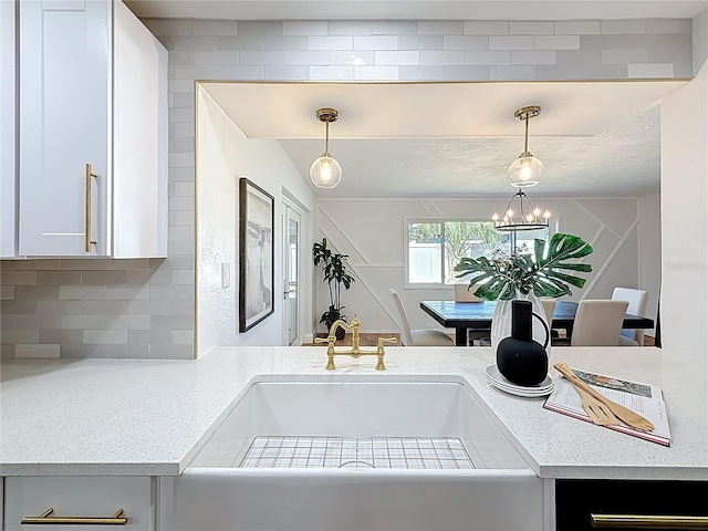 interior space featuring an inviting chandelier, a sink, light countertops, decorative light fixtures, and backsplash