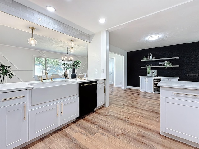 kitchen featuring decorative light fixtures, light countertops, light wood-type flooring, black dishwasher, and a sink