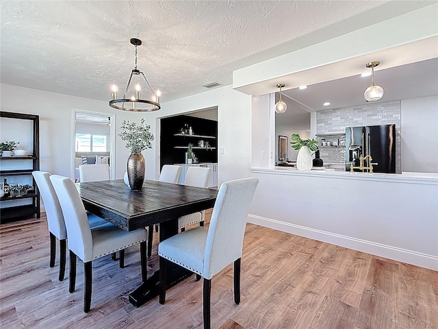 dining space featuring visible vents, a notable chandelier, a textured ceiling, light wood finished floors, and baseboards