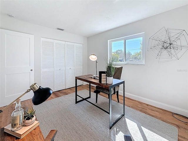 office area with wood finished floors, visible vents, and baseboards