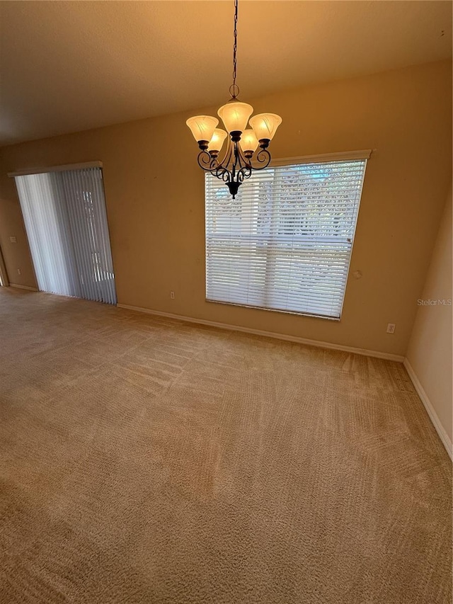 carpeted spare room with a notable chandelier and baseboards