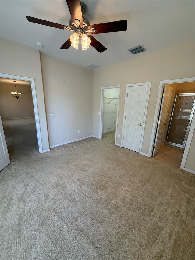 unfurnished bedroom featuring visible vents, ceiling fan with notable chandelier, ensuite bath, baseboards, and light colored carpet