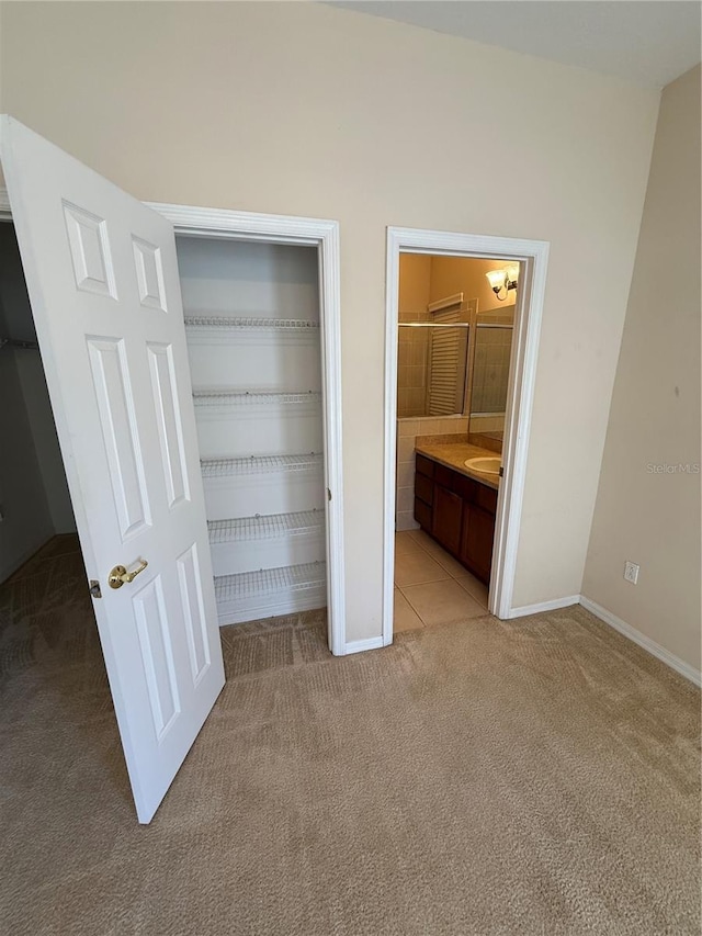 unfurnished bedroom featuring light carpet, connected bathroom, baseboards, and a closet