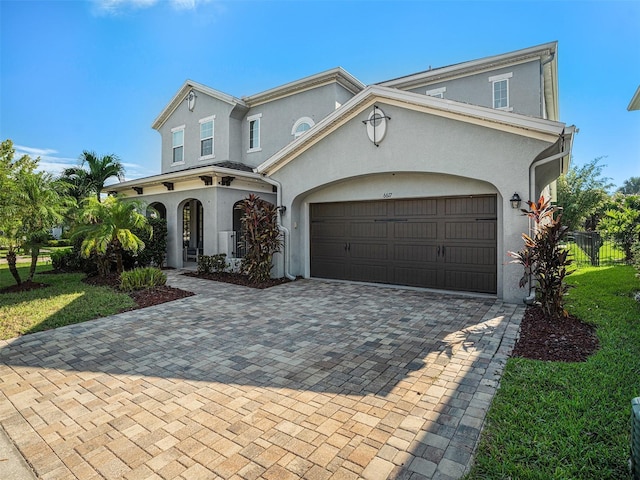 mediterranean / spanish-style home with stucco siding, decorative driveway, fence, a front yard, and an attached garage