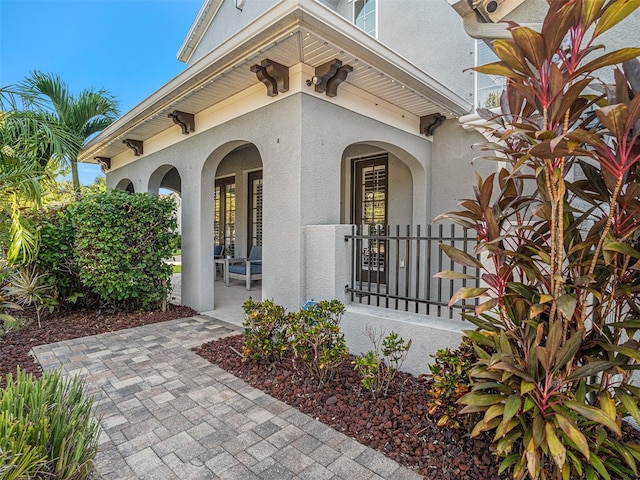 property entrance with stucco siding, a porch, and fence