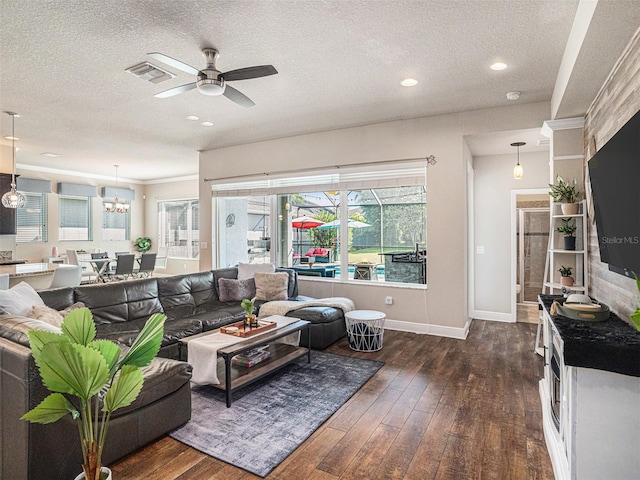 living area with dark wood-style floors, baseboards, visible vents, a textured ceiling, and ceiling fan with notable chandelier