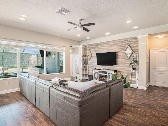 living area with visible vents, a ceiling fan, wood finished floors, a glass covered fireplace, and an accent wall