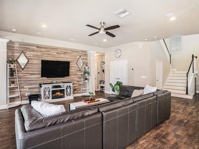 living area with stairway, wood finished floors, a ceiling fan, visible vents, and an accent wall