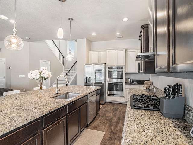 kitchen with dark brown cabinets, dark wood finished floors, light stone counters, appliances with stainless steel finishes, and a sink