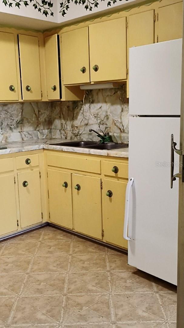 kitchen with tasteful backsplash, cream cabinets, light countertops, and freestanding refrigerator