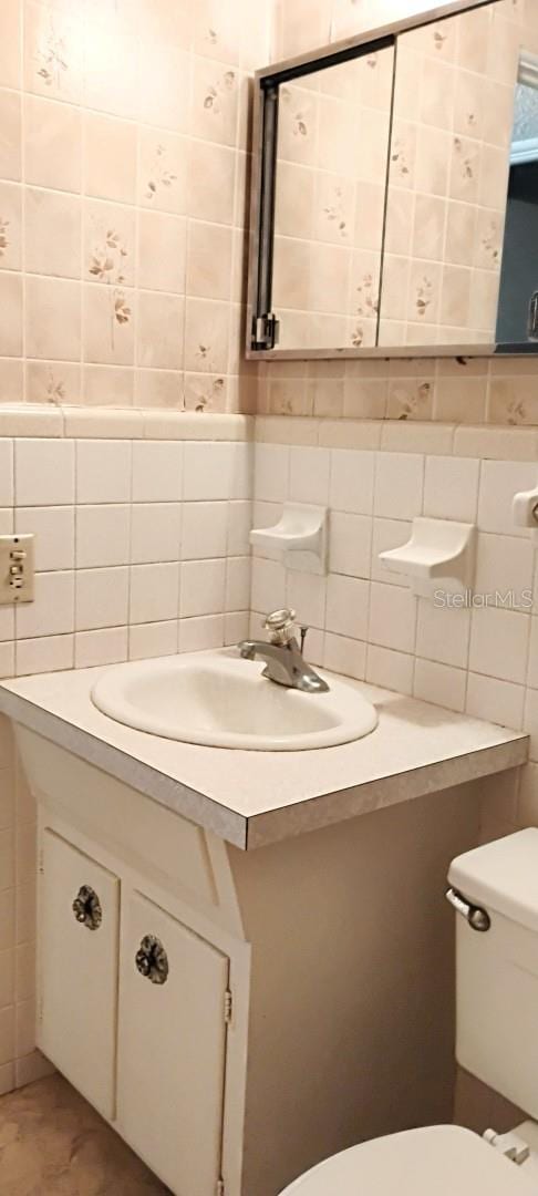 half bath with backsplash, vanity, toilet, and tile walls