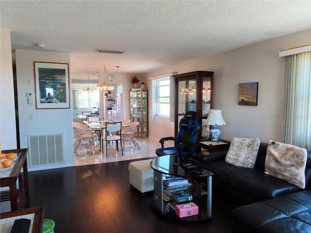 living room with visible vents, a textured ceiling, wood finished floors, and a chandelier