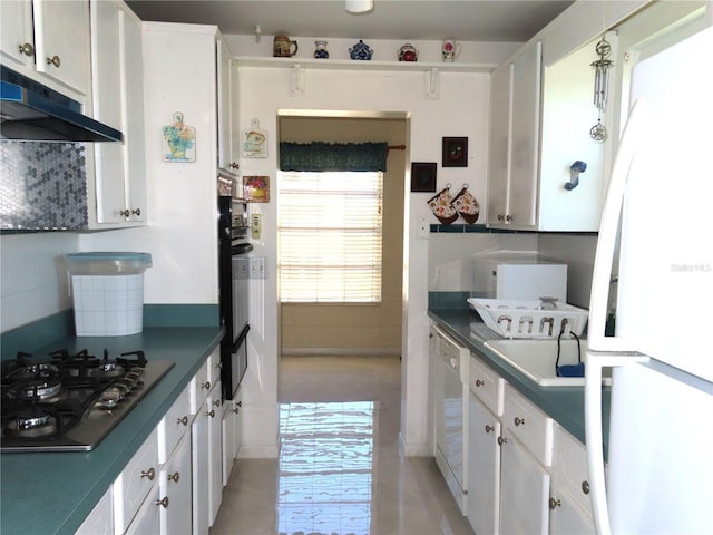 kitchen with dark countertops, under cabinet range hood, decorative backsplash, white cabinets, and white appliances