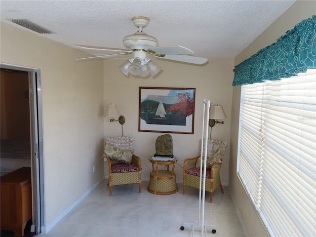 sitting room with baseboards, visible vents, light tile patterned flooring, ceiling fan, and a textured ceiling