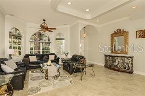 living area with baseboards, a raised ceiling, ornamental molding, and a ceiling fan