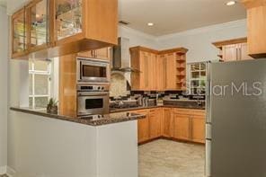 kitchen featuring a peninsula, open shelves, glass insert cabinets, appliances with stainless steel finishes, and wall chimney exhaust hood