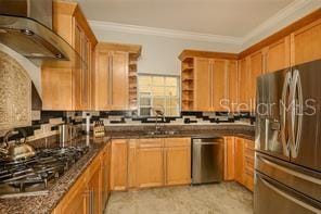 kitchen with open shelves, stainless steel appliances, crown molding, wall chimney range hood, and tasteful backsplash