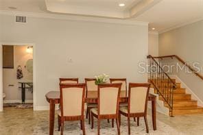 dining room featuring stairs, a tray ceiling, baseboards, and ornamental molding