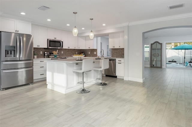 kitchen featuring visible vents, backsplash, a kitchen island, arched walkways, and appliances with stainless steel finishes