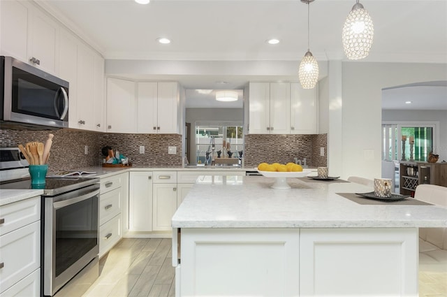 kitchen featuring arched walkways, white cabinetry, appliances with stainless steel finishes, and a center island