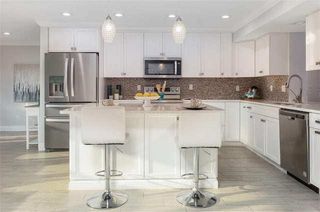 kitchen featuring a kitchen island, ornamental molding, decorative backsplash, appliances with stainless steel finishes, and white cabinetry