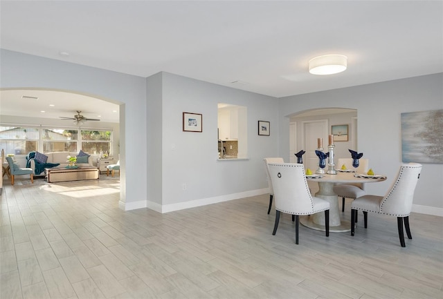 dining room with light wood-type flooring, visible vents, a ceiling fan, arched walkways, and baseboards