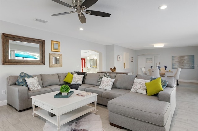 living room featuring arched walkways, recessed lighting, light wood-type flooring, and baseboards