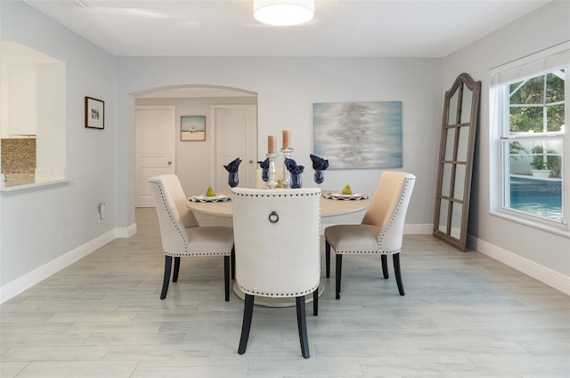 dining area with arched walkways, light wood-type flooring, and baseboards