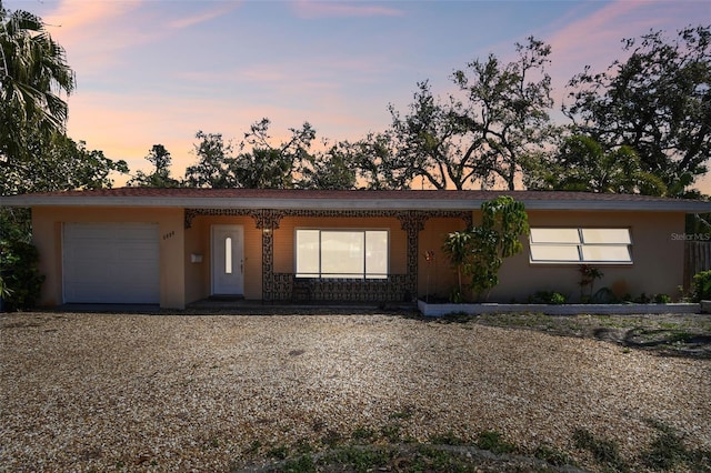 ranch-style house featuring a garage, gravel driveway, covered porch, and stucco siding