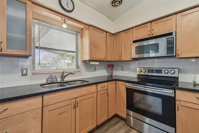 kitchen with a sink, dark stone countertops, backsplash, and stainless steel appliances