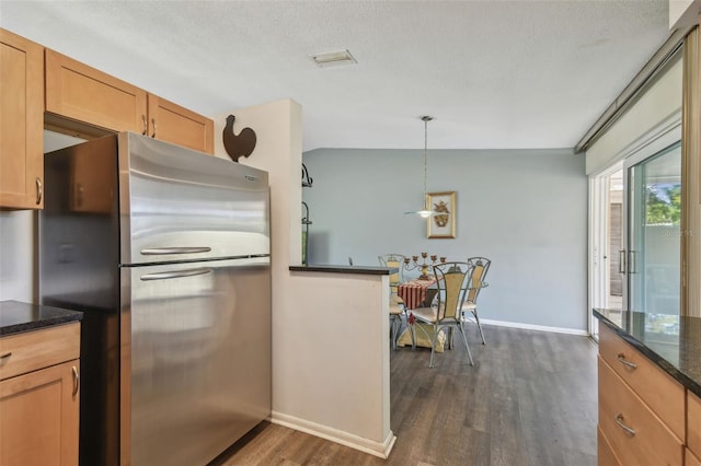 kitchen featuring hanging light fixtures, dark stone countertops, dark wood-style flooring, and freestanding refrigerator