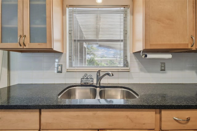 kitchen featuring light brown cabinetry, backsplash, glass insert cabinets, and a sink