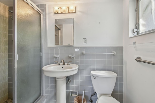 bathroom with a shower stall, toilet, tile walls, and wainscoting