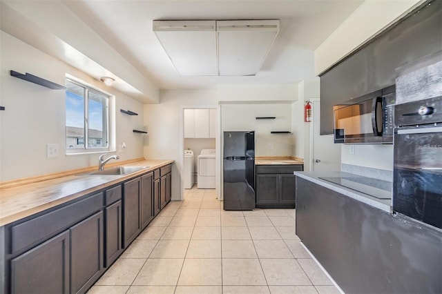 kitchen with washing machine and clothes dryer, wooden counters, light tile patterned flooring, black appliances, and a sink