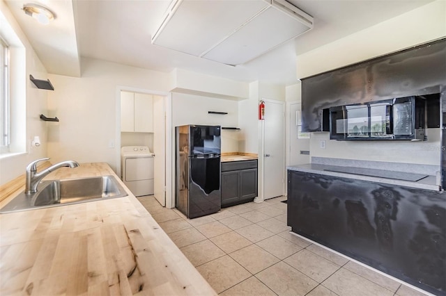 kitchen with washer / clothes dryer, light tile patterned flooring, butcher block countertops, a sink, and black appliances