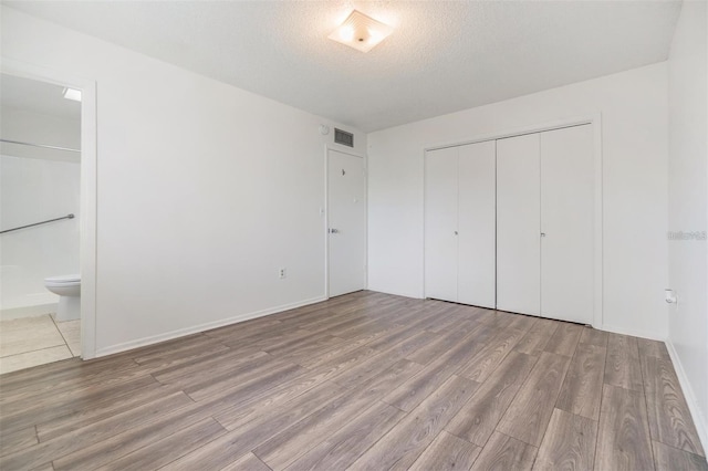 unfurnished bedroom with visible vents, ensuite bath, wood finished floors, a closet, and a textured ceiling