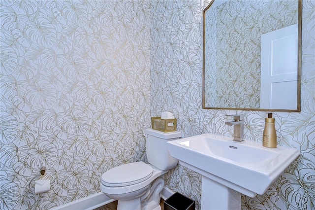 half bathroom with toilet, wallpapered walls, and a sink