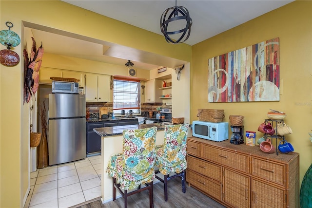 kitchen featuring backsplash, light tile patterned floors, a peninsula, stainless steel appliances, and white cabinetry