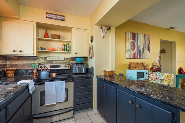 kitchen featuring white microwave, stainless steel electric range oven, dark stone counters, and light tile patterned flooring