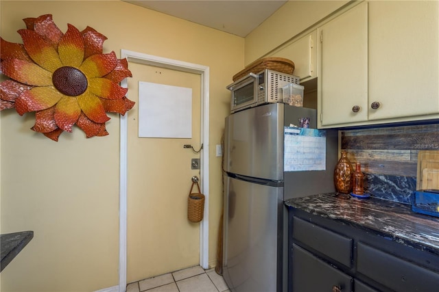 kitchen with dark countertops, cream cabinets, light tile patterned floors, and freestanding refrigerator