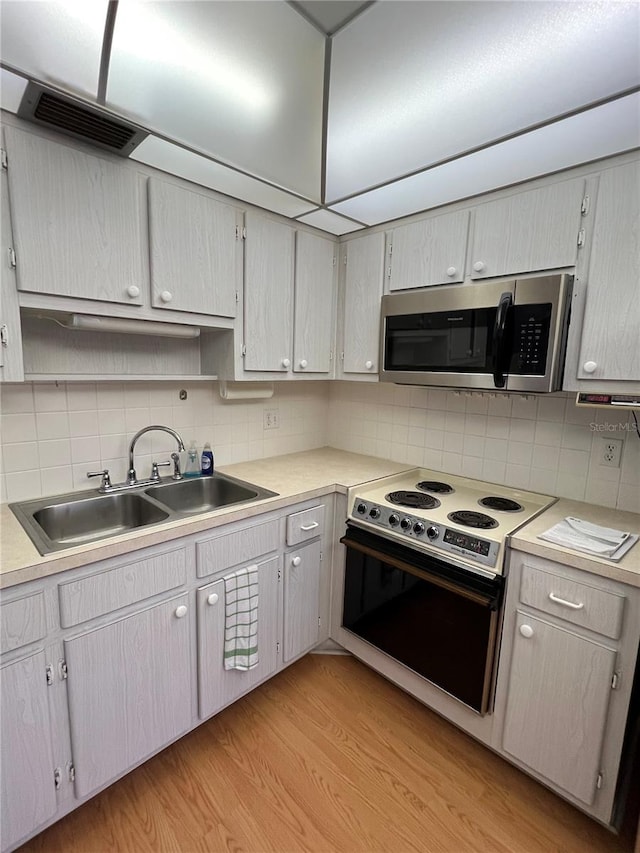 kitchen with visible vents, a sink, stainless steel microwave, range with electric stovetop, and light wood finished floors