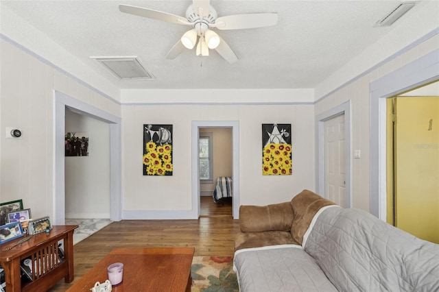 living area featuring a ceiling fan, wood finished floors, visible vents, and a textured ceiling