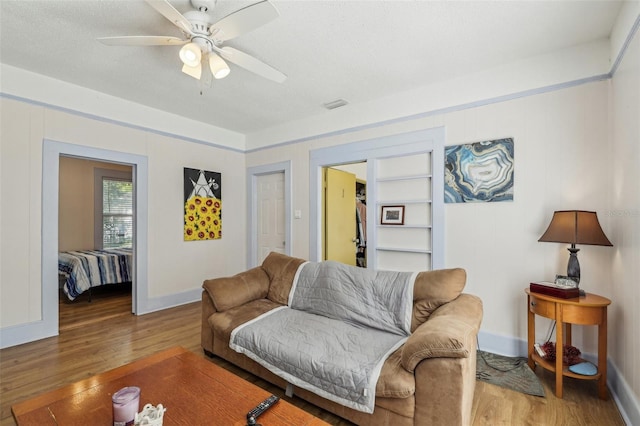 living area featuring ceiling fan, visible vents, baseboards, and wood finished floors