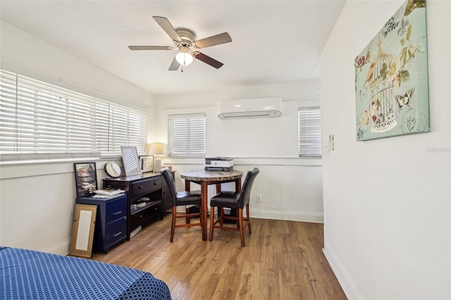 bedroom featuring a wall mounted air conditioner, baseboards, ceiling fan, and light wood finished floors