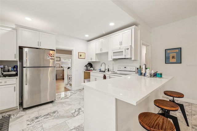 kitchen featuring marble finish floor, white appliances, a breakfast bar, and a peninsula