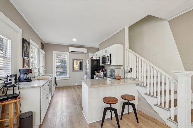 kitchen featuring a sink, stainless steel appliances, an AC wall unit, light wood-style floors, and a kitchen breakfast bar