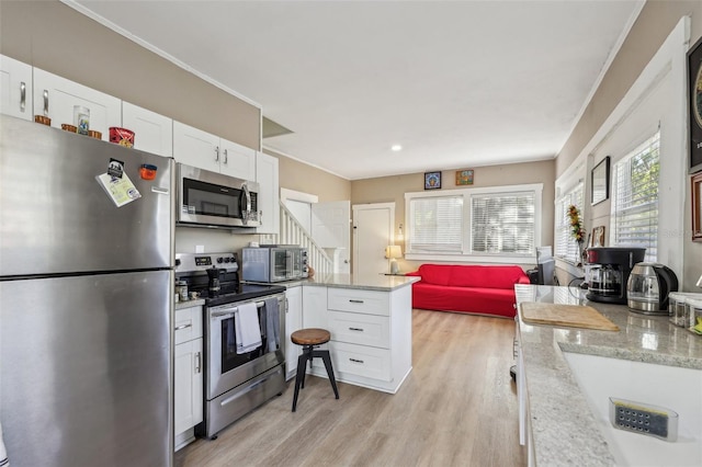 kitchen with light wood-type flooring, light stone counters, stainless steel appliances, a peninsula, and white cabinets