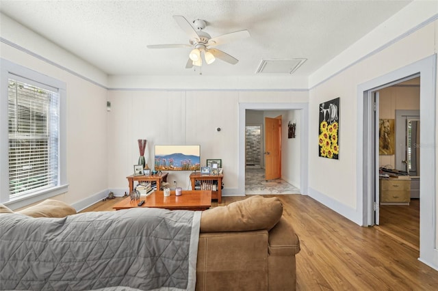 living area featuring baseboards, light wood-style flooring, a textured ceiling, and ceiling fan