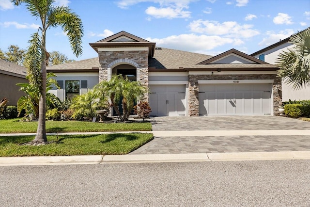 view of front of home featuring stucco siding, a front lawn, decorative driveway, stone siding, and a garage